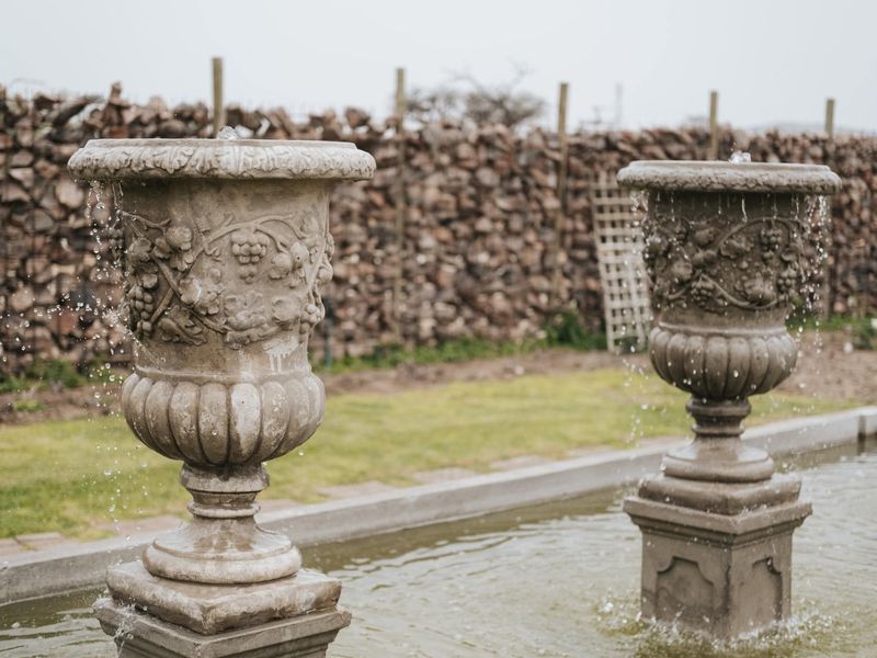 A well-maintained garden area featuring decorative stone water fountains set against a rustic stone retaining wall.