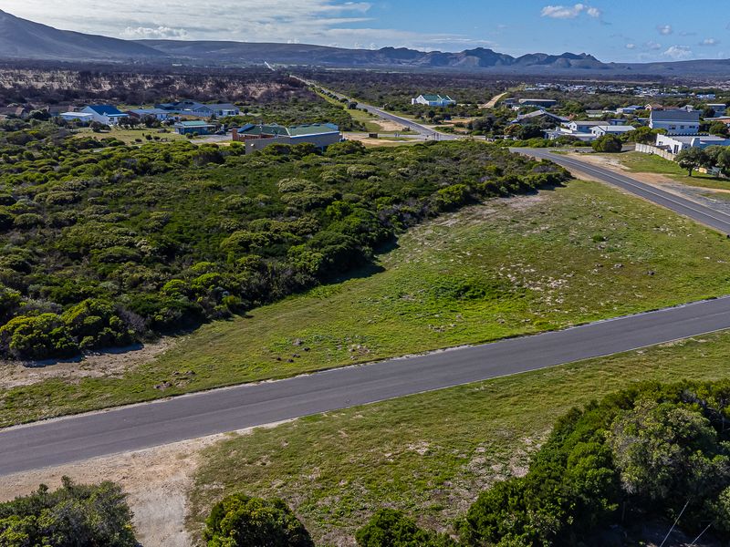 An aerial view of a vacant residential plot featuring natural vegetation and adjacent paved road access in a coastal landscape setting.