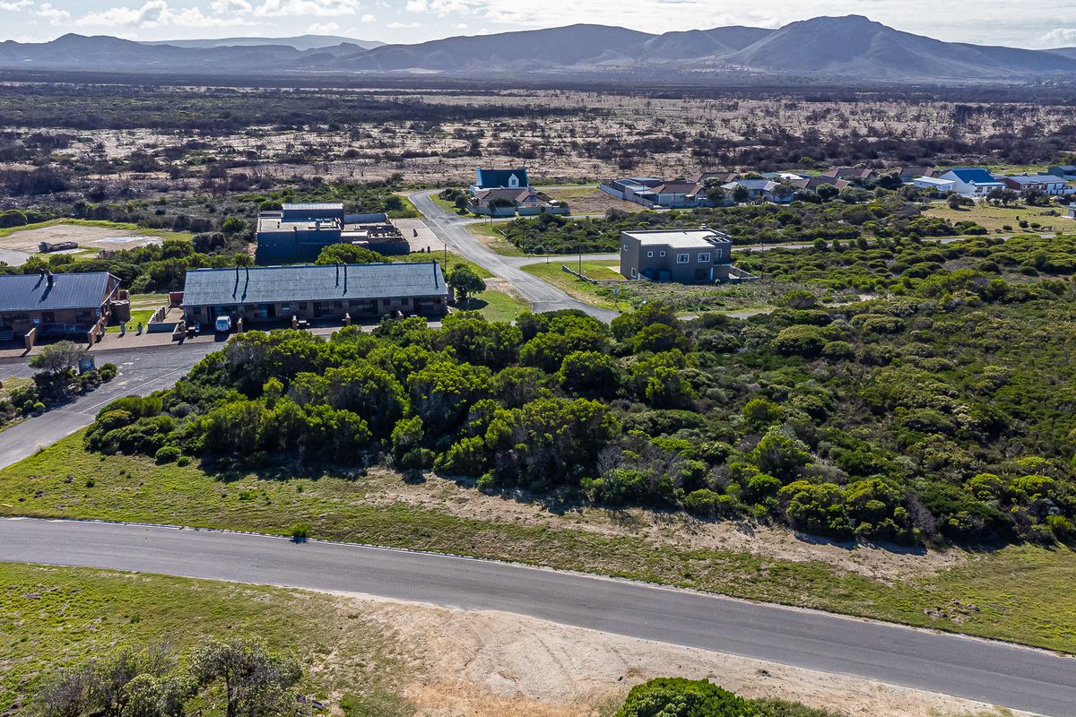 An aerial view of a vacant residential plot surrounded by coastal vegetation, paved roads, and existing residential properties in a scenic landscape.