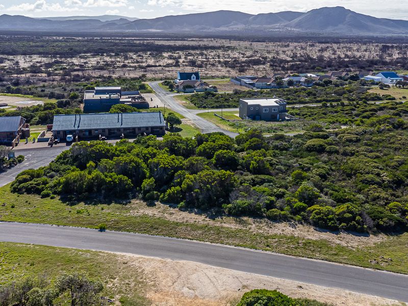 An aerial view of a vacant residential plot surrounded by coastal vegetation, paved roads, and existing residential properties in a scenic landscape.