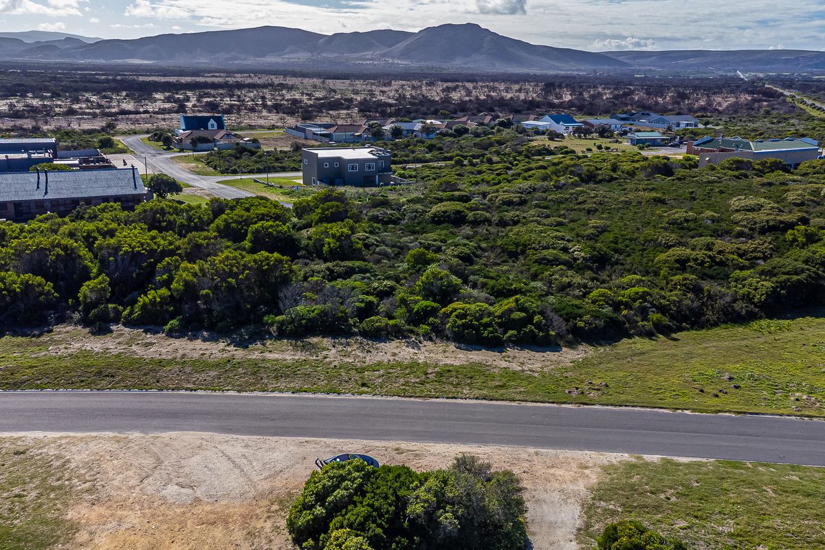 Aerial view of a vacant residential plot featuring native vegetation and adjacent paved road access in a coastal estate setting.