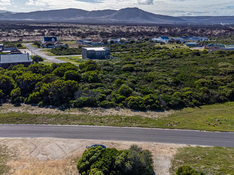 Aerial view of a vacant residential plot featuring native vegetation and adjacent paved road access in a coastal estate setting.