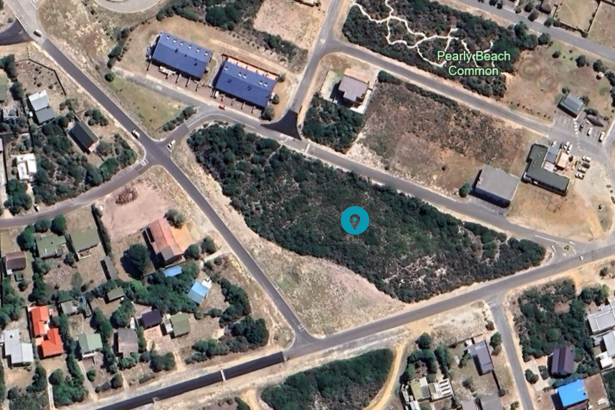 An aerial view of a vacant residential plot situated within a developed coastal neighborhood, featuring natural vegetation and surrounding road infrastructure.