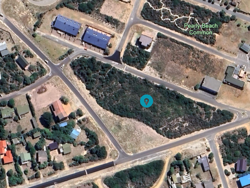 An aerial view of a vacant residential plot situated within a developed coastal neighborhood, featuring natural vegetation and surrounding road infrastructure.