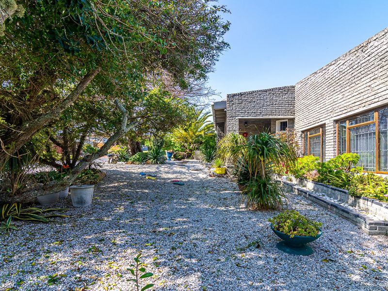 A rear exterior view of the property featuring a gravel garden area, mature trees, and a textured brick facade.