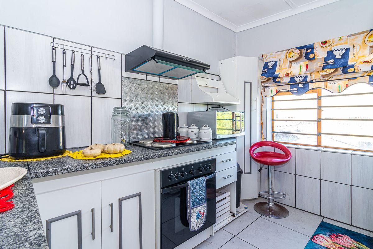 A functional kitchen featuring granite countertops, built-in oven with hob, extractor fan, and tiled splashbacks, offering a practical layout for daily meal preparation.