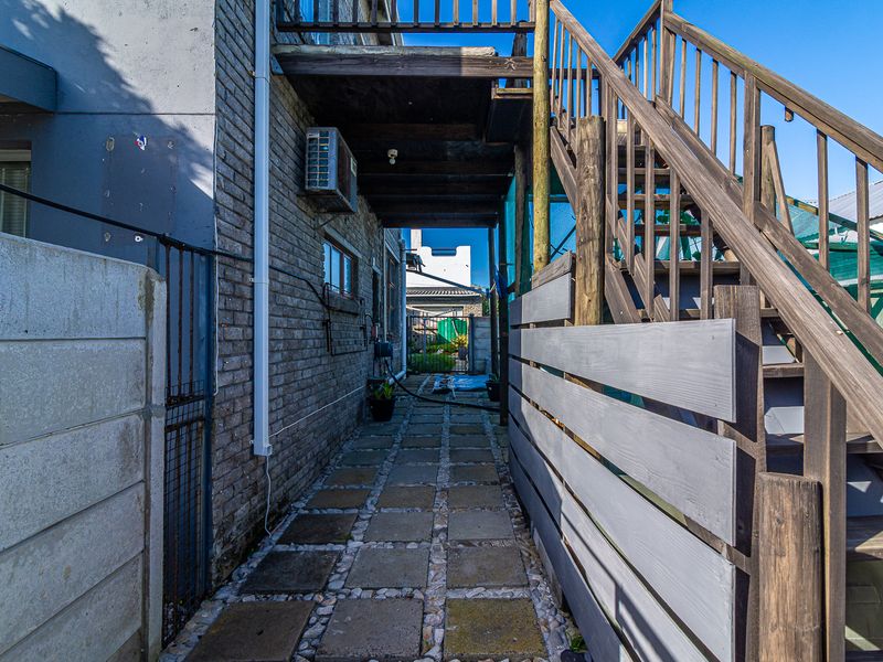 A side exterior walkway featuring a timber staircase, brick walling, and paved path leading to the rear of the property.