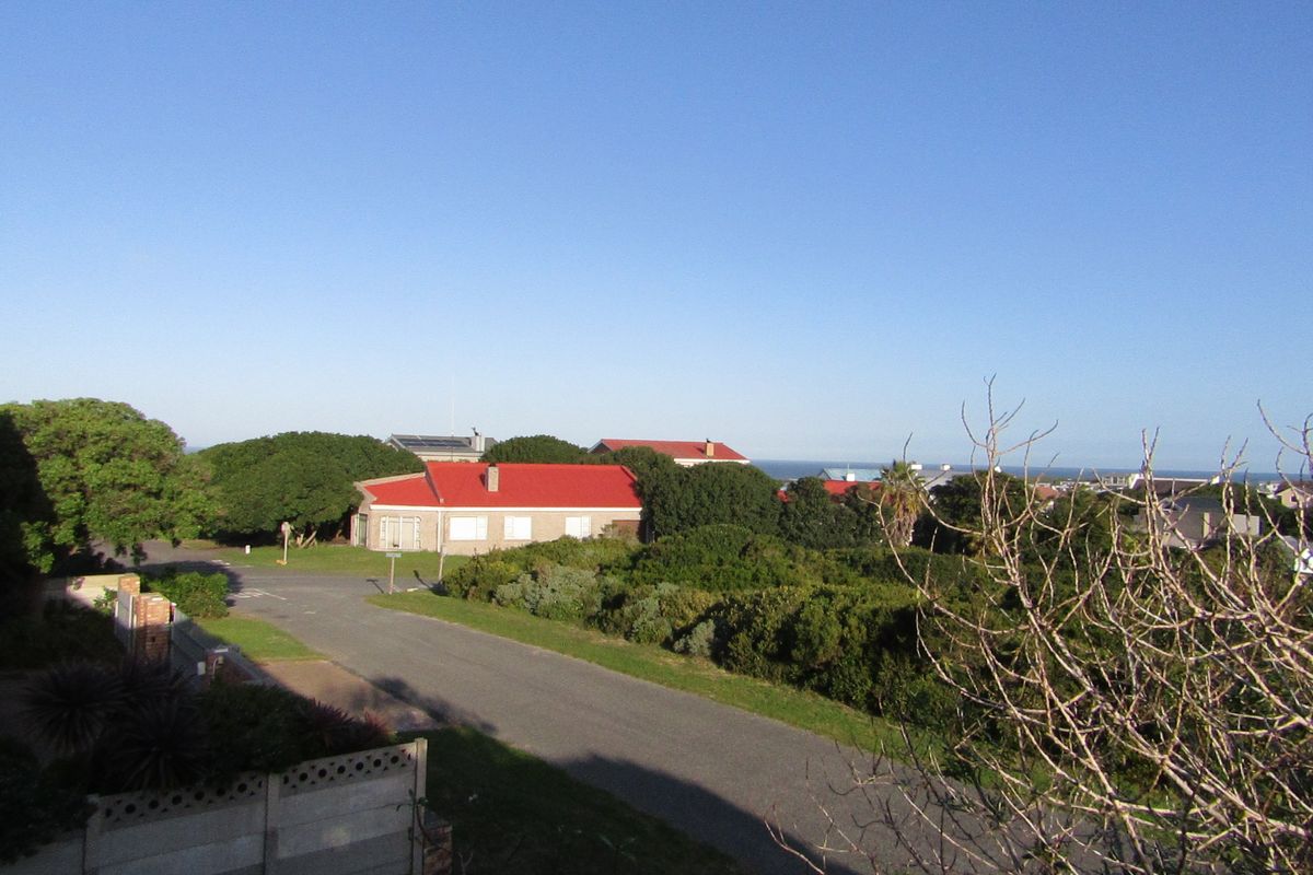 An elevated aerial view of a residential street and surrounding coastal neighborhood landscape under a clear blue sky.