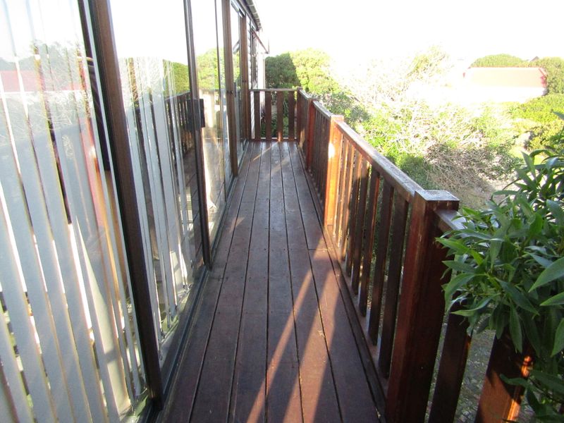 A narrow timber balcony featuring a wooden balustrade and sliding glass door access, overlooking the surrounding garden area.