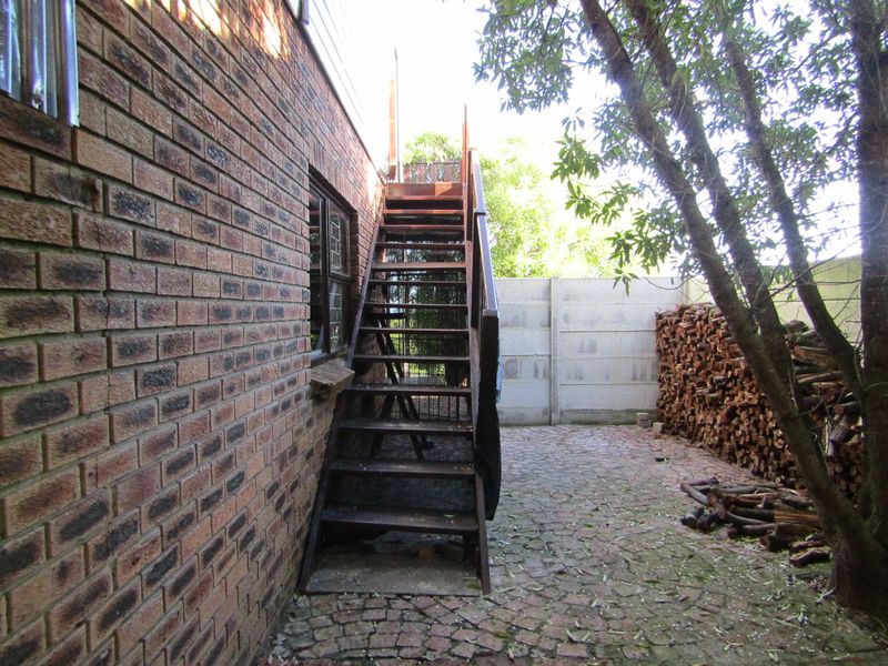 Rear exterior view featuring a brick facade, an external timber staircase, and a paved courtyard area enclosed by a concrete boundary wall.