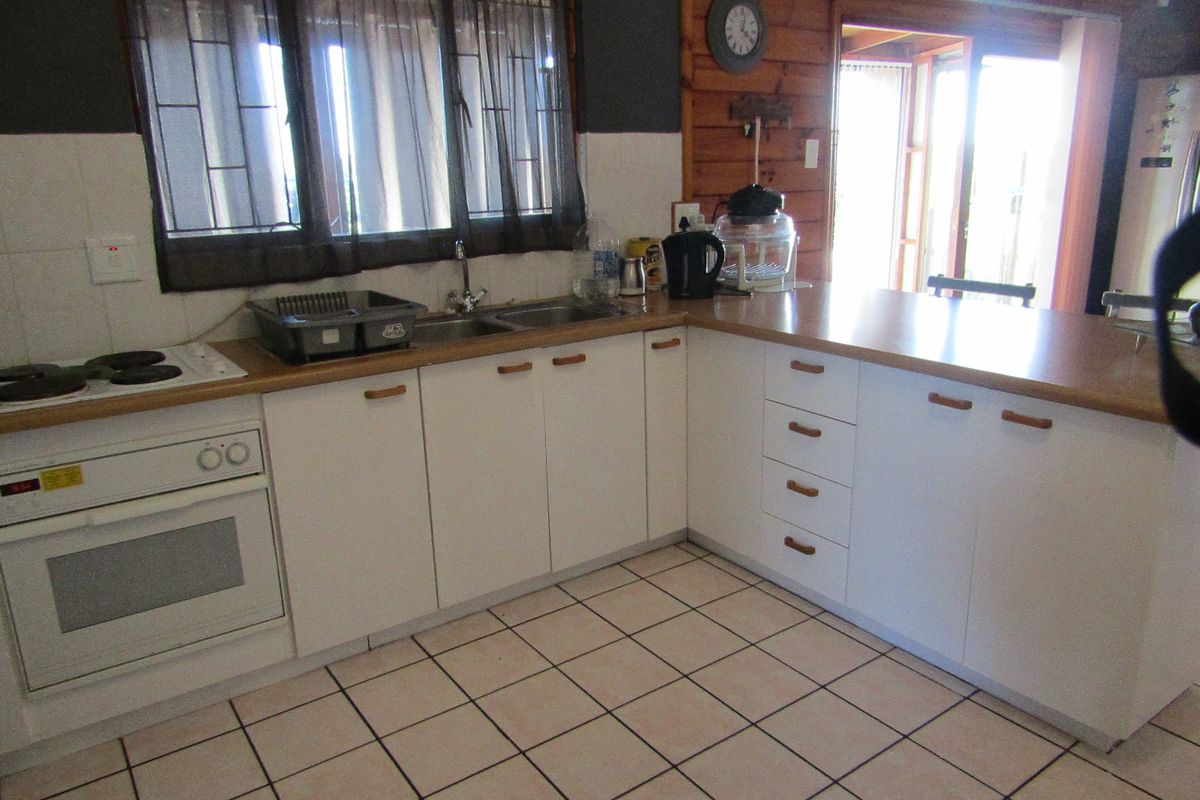 Functional kitchen featuring white cabinetry, laminate countertops, built-in oven, electric hob, and tiled flooring with timber wall accents.
