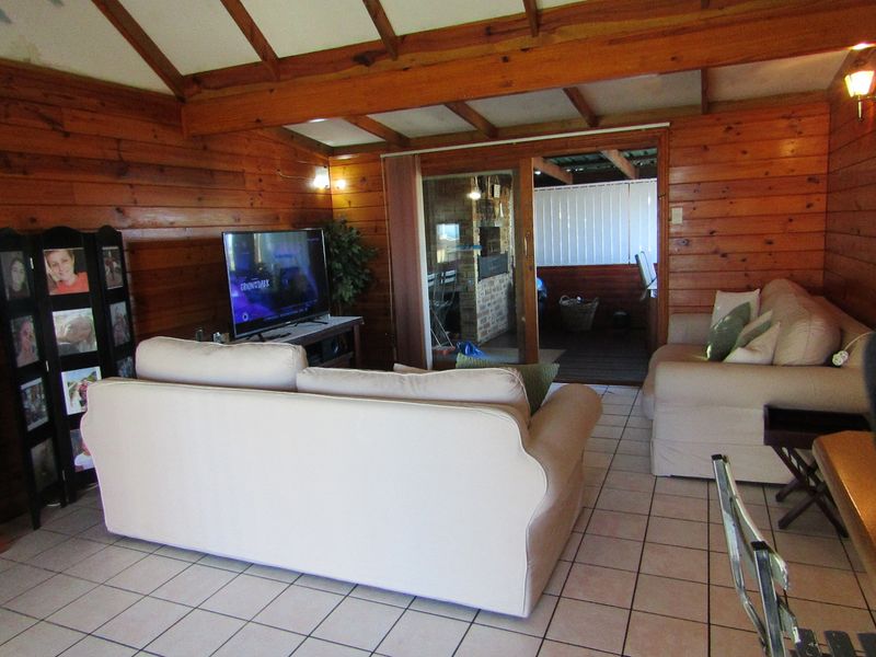 Living room featuring exposed timber ceiling beams, timber wall cladding, and tiled flooring, with a sliding glass door leading to an outdoor area.