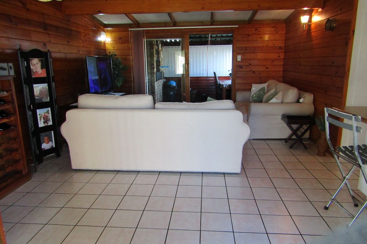 A living room featuring warm timber wall paneling, exposed ceiling beams, and ceramic tiled flooring, with a sliding glass door leading to an outdoor area.