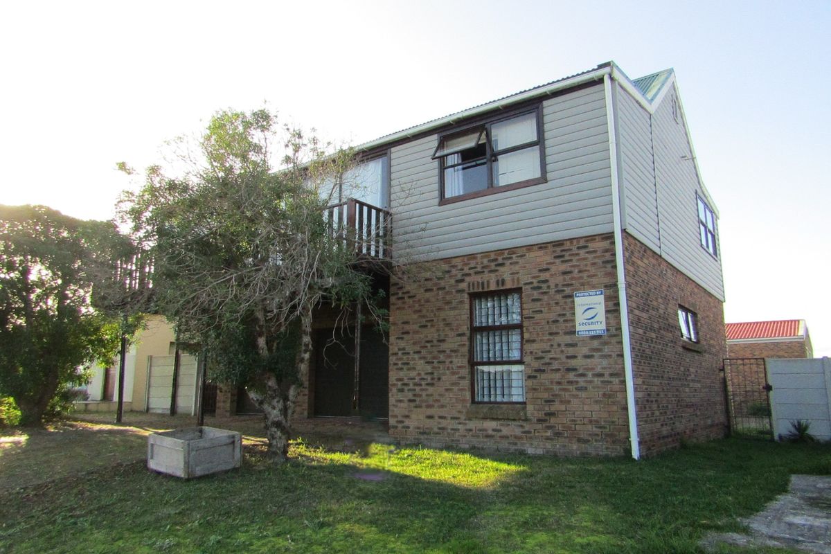 Rear view of a two-story house featuring a brick lower level, timber-clad upper level, and a small balcony.