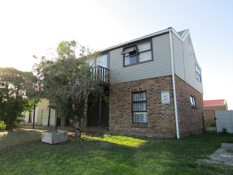 Rear view of a two-story house featuring a brick lower level, timber-clad upper level, and a small balcony.