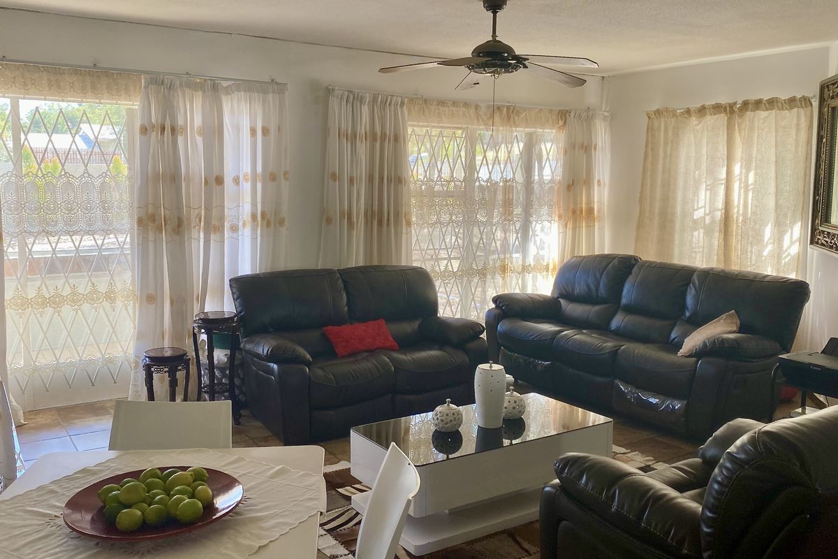 Spacious open-plan living and dining area featuring tiled flooring, a ceiling fan, and large windows with security gates for natural light.