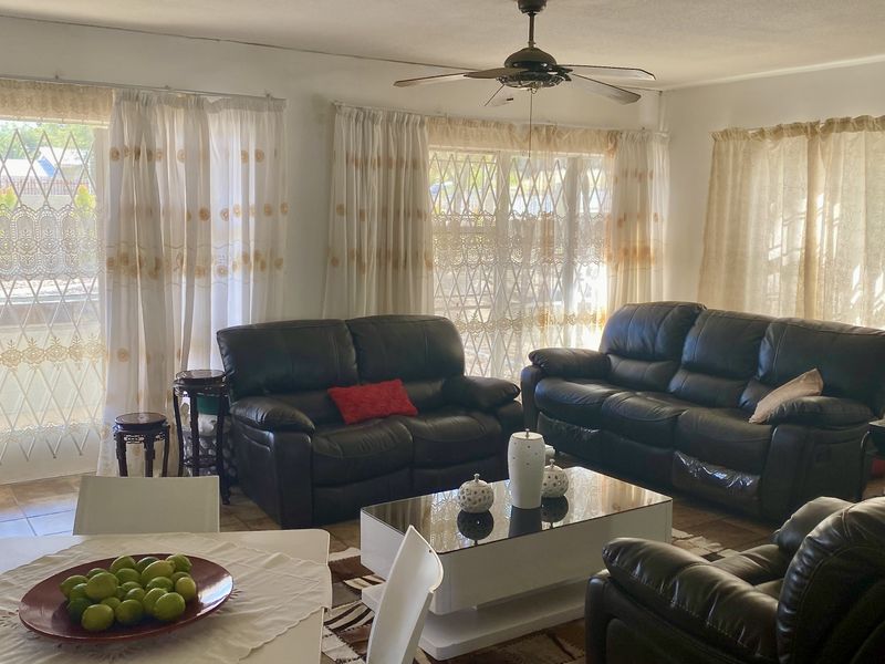 Spacious open-plan living and dining area featuring tiled flooring, a ceiling fan, and large windows with security gates for natural light.