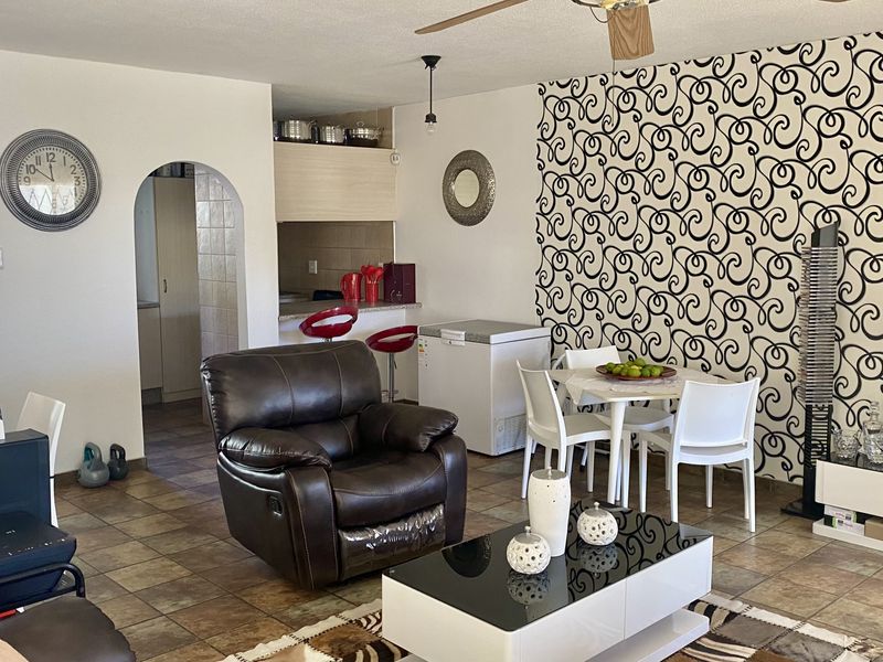 Open plan living and dining area featuring tiled flooring, a ceiling fan, and an arched entryway leading to the kitchen space.
