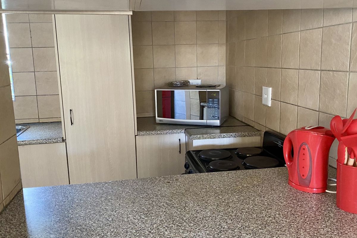 A functional kitchen featuring granite countertops, ceramic wall tiling, built-in cabinetry, and an electric stove.