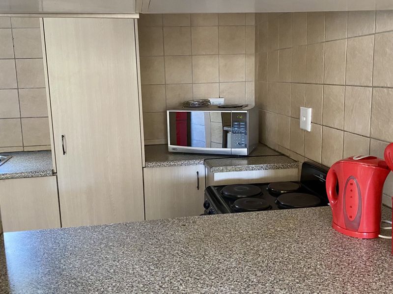 A functional kitchen featuring granite countertops, ceramic wall tiling, built-in cabinetry, and an electric stove.