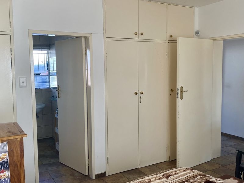 Bedroom featuring built-in cupboards with dated finishes and tiled flooring, providing access to an adjoining bathroom and hallway.