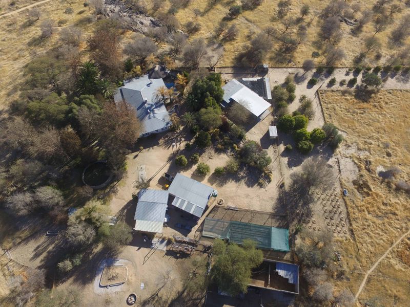 Aerial view of a small holding property featuring multiple outbuildings, fenced enclosures, and established trees set within a rural landscape.