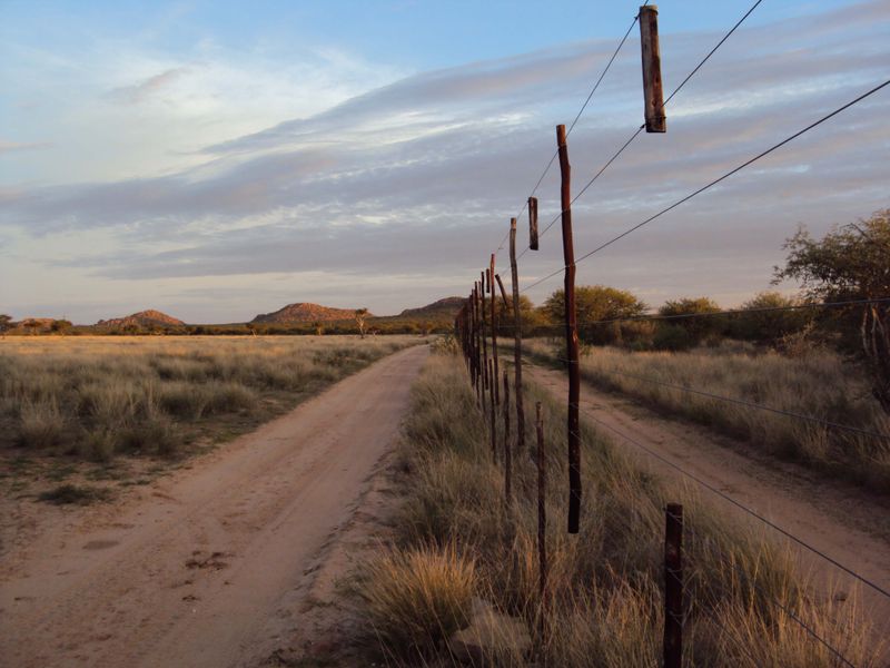 A scenic view of the small holding property featuring a dirt access track and traditional wire fencing against a natural landscape backdrop.