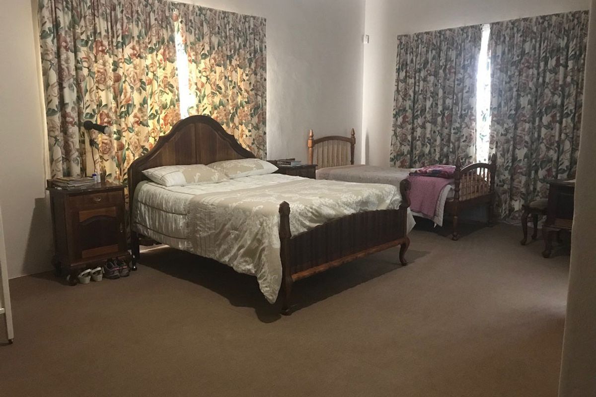 Spacious bedroom featuring neutral walls, carpeted flooring, and large windows with floor-to-ceiling curtains.