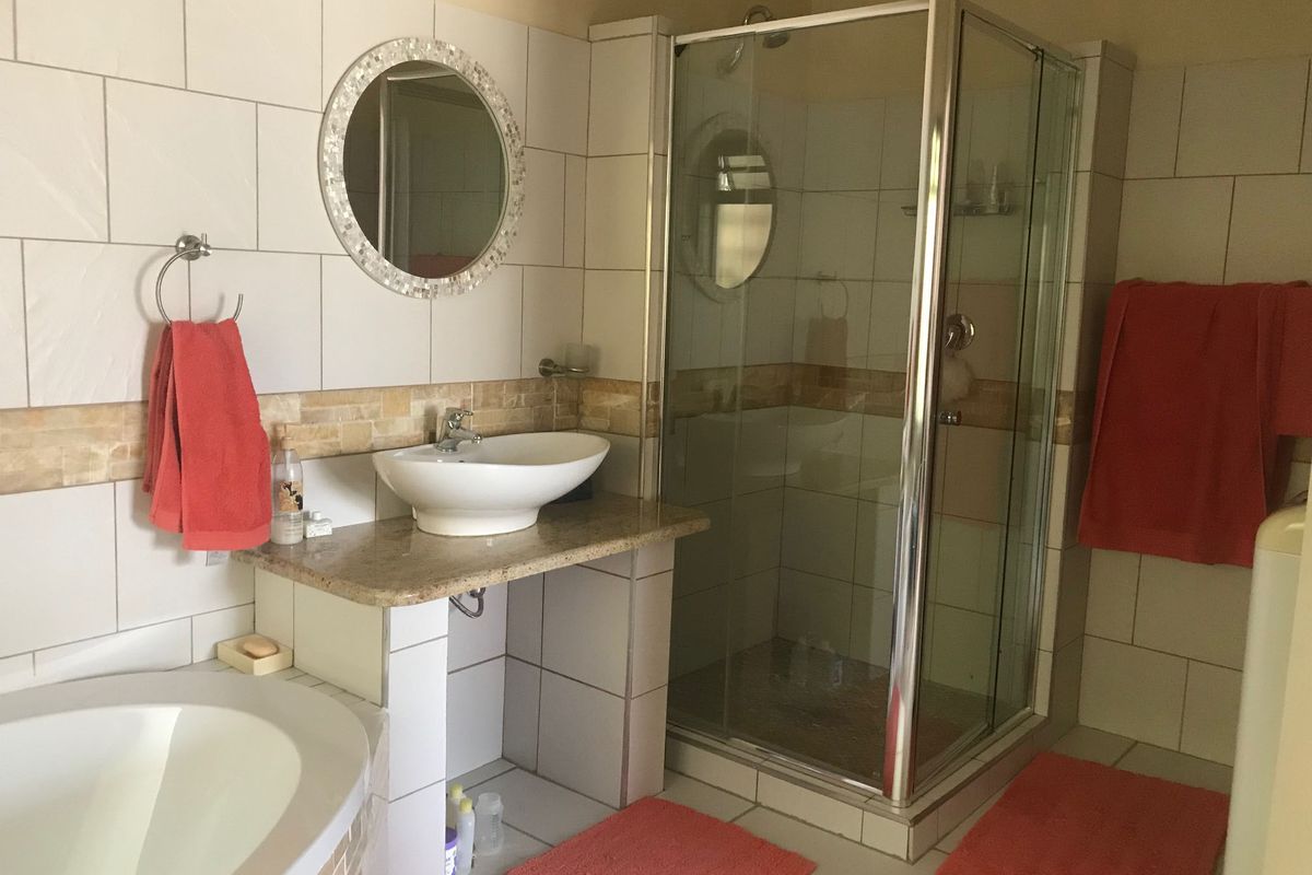 A well-maintained bathroom featuring a glass shower enclosure, a vessel sink on a granite vanity, and a built-in bathtub with neutral wall tiling.