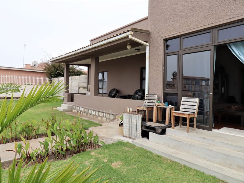 A covered patio area featuring concrete steps, stone base detailing, and aluminium sliding doors leading into the home, set against a landscaped garden.