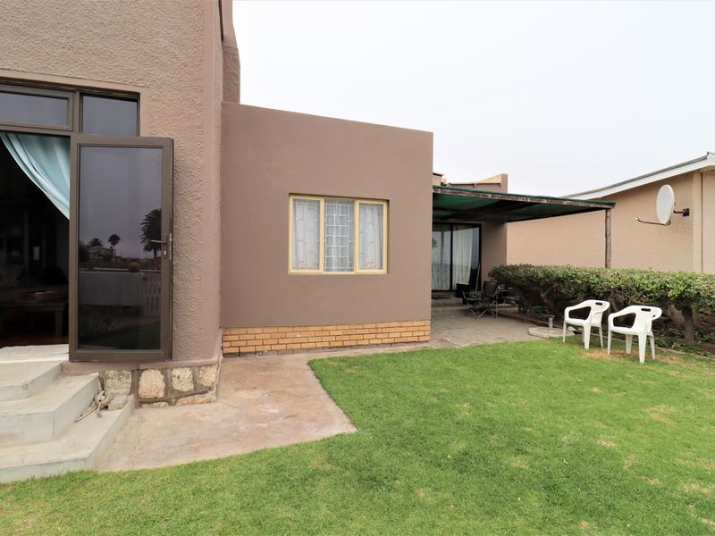 Rear exterior view featuring a small lawn, covered patio area, and direct access to the living space via sliding glass doors.