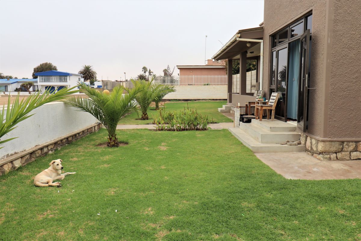 A rear view of the property featuring a well-maintained lawn, stone-clad exterior accents, and a concrete patio area accessible via sliding glass doors.