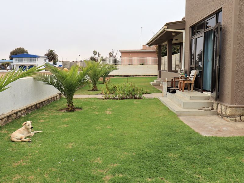 A rear view of the property featuring a well-maintained lawn, stone-clad exterior accents, and a concrete patio area accessible via sliding glass doors.
