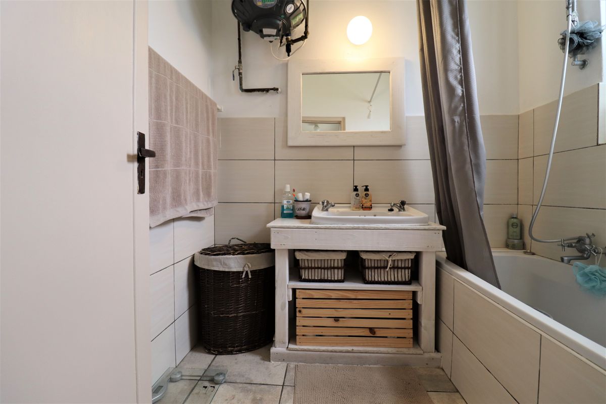 A functional bathroom featuring a vanity unit with a ceramic basin, a bathtub with shower mixer, and wall-mounted water heater.