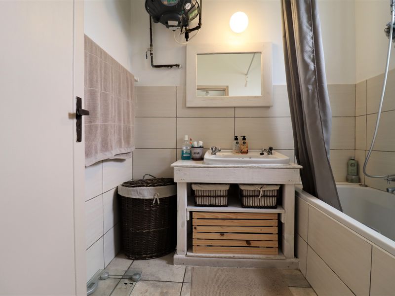 A functional bathroom featuring a vanity unit with a ceramic basin, a bathtub with shower mixer, and wall-mounted water heater.
