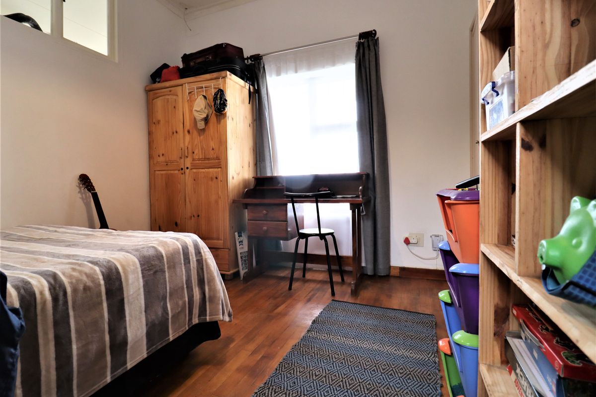 A functional bedroom featuring hardwood flooring and natural light from a window, providing a comfortable space for rest or study.