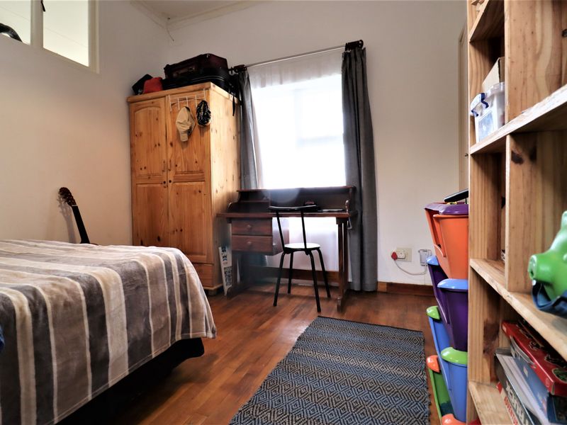 A functional bedroom featuring hardwood flooring and natural light from a window, providing a comfortable space for rest or study.