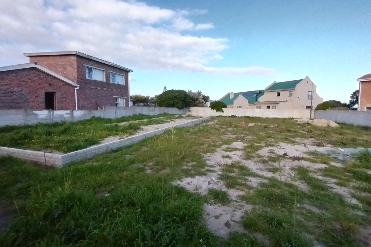 A vacant residential plot featuring a concrete boundary wall and an existing brick foundation slab, ready for development.