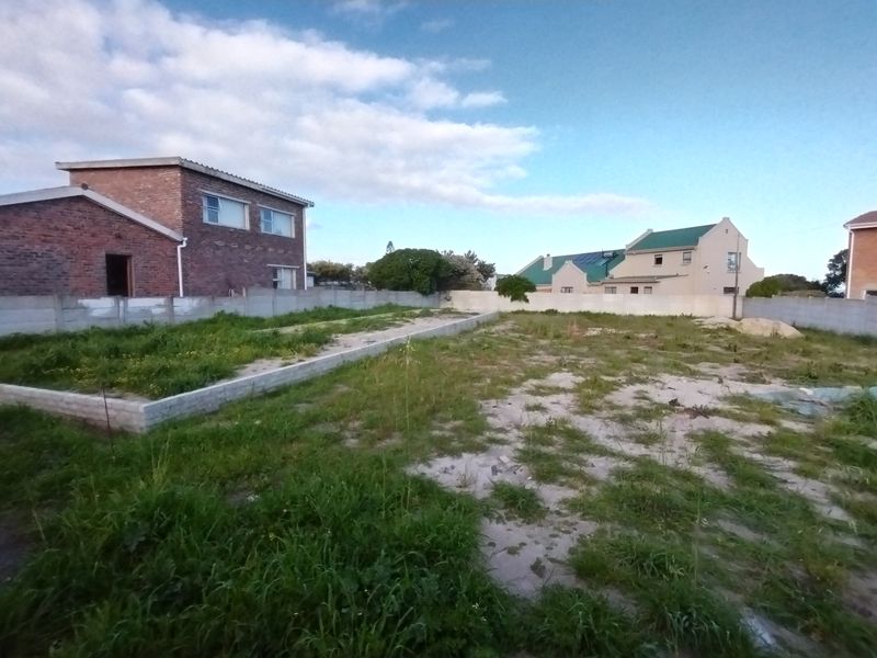 A vacant residential plot featuring a concrete boundary wall and an existing brick foundation slab, ready for development.