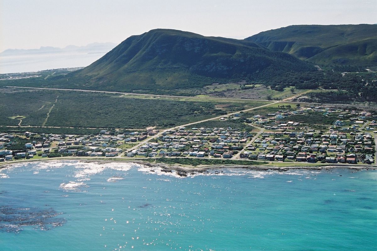 An aerial view of a coastal residential neighborhood situated between the ocean and mountain ranges.
