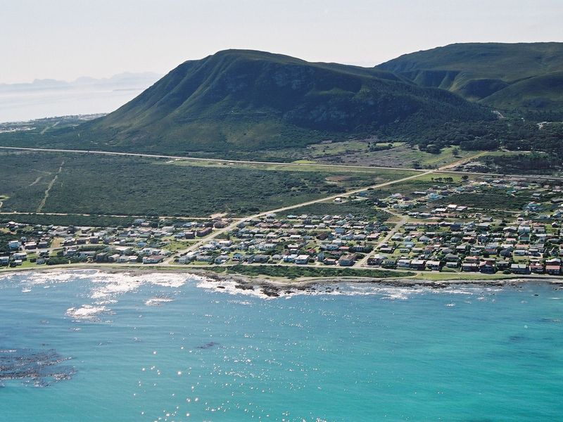 An aerial view of a coastal residential neighborhood situated between the ocean and mountain ranges.