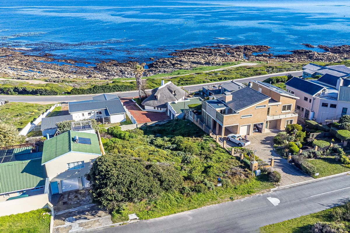 Aerial view of a coastal residential neighborhood featuring multiple homes, paved driveways, and proximity to the rocky shoreline.