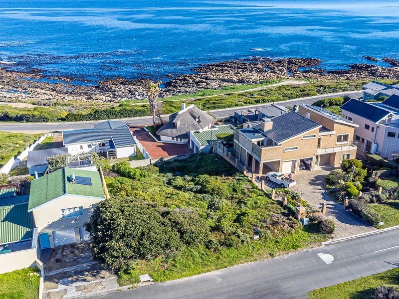 Aerial view of a coastal residential neighborhood featuring multiple homes, paved driveways, and proximity to the rocky shoreline.