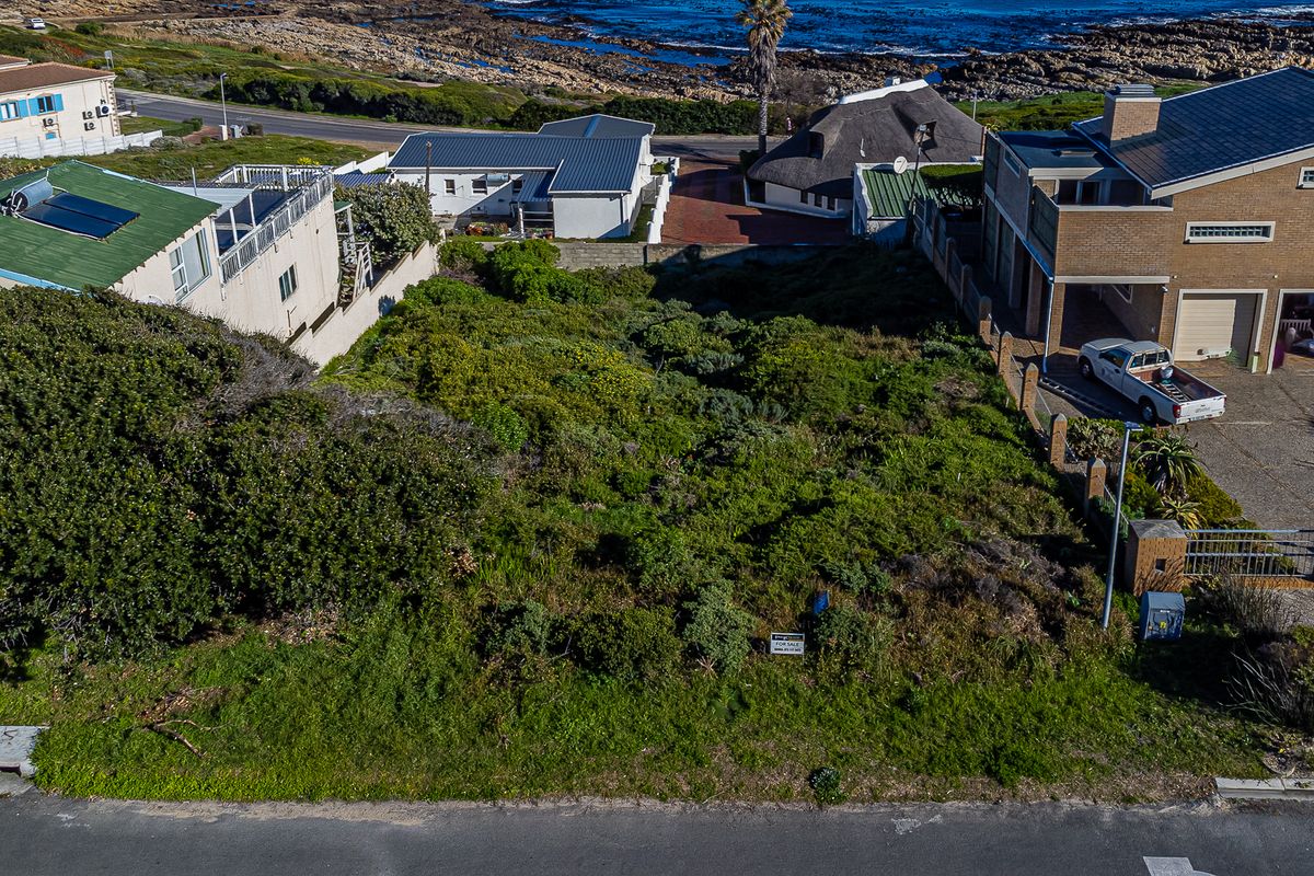 An aerial view of a vacant residential plot situated in a coastal neighborhood, surrounded by established homes and offering proximity to the ocean.