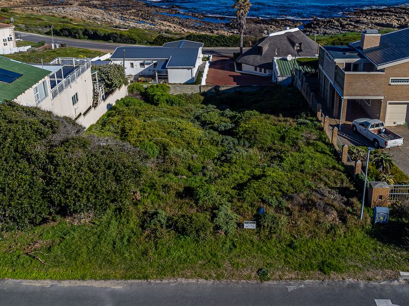 An aerial view of a vacant residential plot situated in a coastal neighborhood, surrounded by established homes and offering proximity to the ocean.