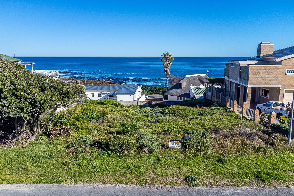 An elevated view of a vacant residential plot featuring coastal scenery and surrounding established properties.