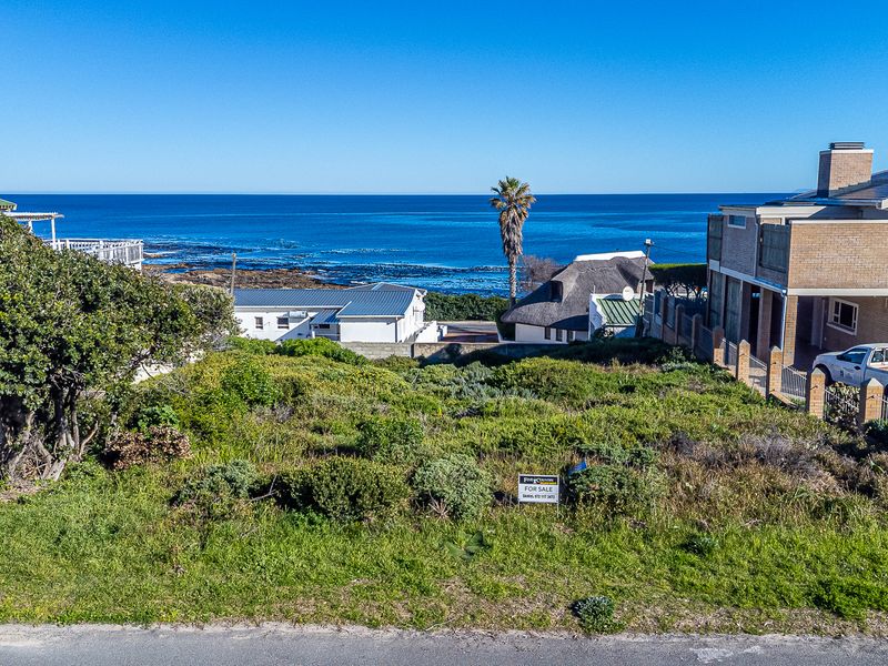 An elevated view of a vacant residential plot featuring coastal scenery and surrounding established properties.
