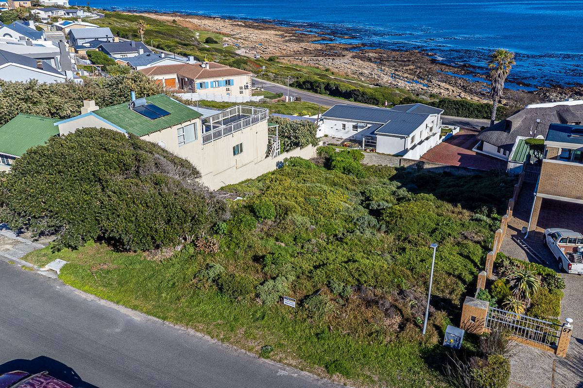 An aerial view of a vacant residential plot situated in a coastal neighborhood, offering potential for development with proximity to the ocean.