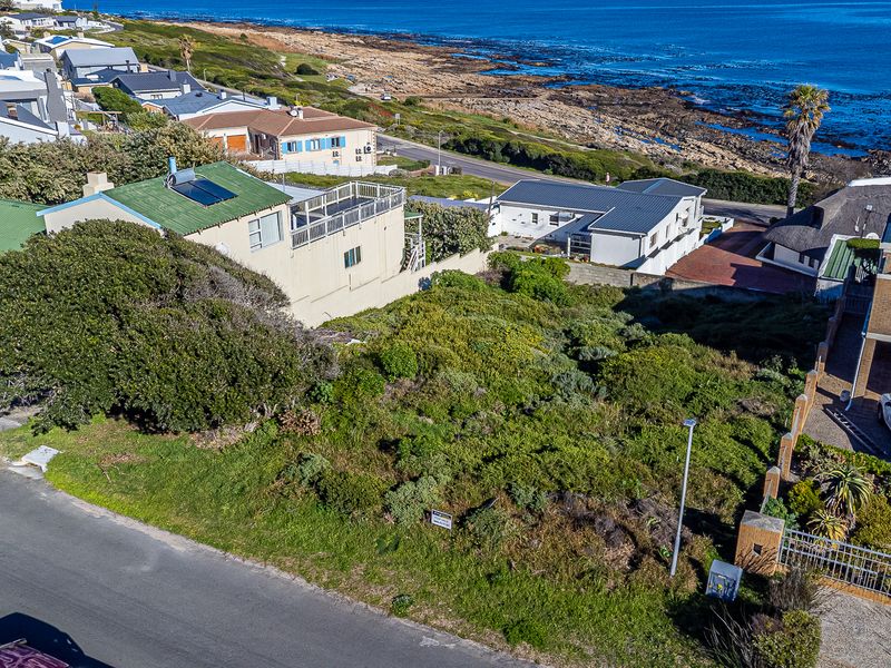 An aerial view of a vacant residential plot situated in a coastal neighborhood, offering potential for development with proximity to the ocean.