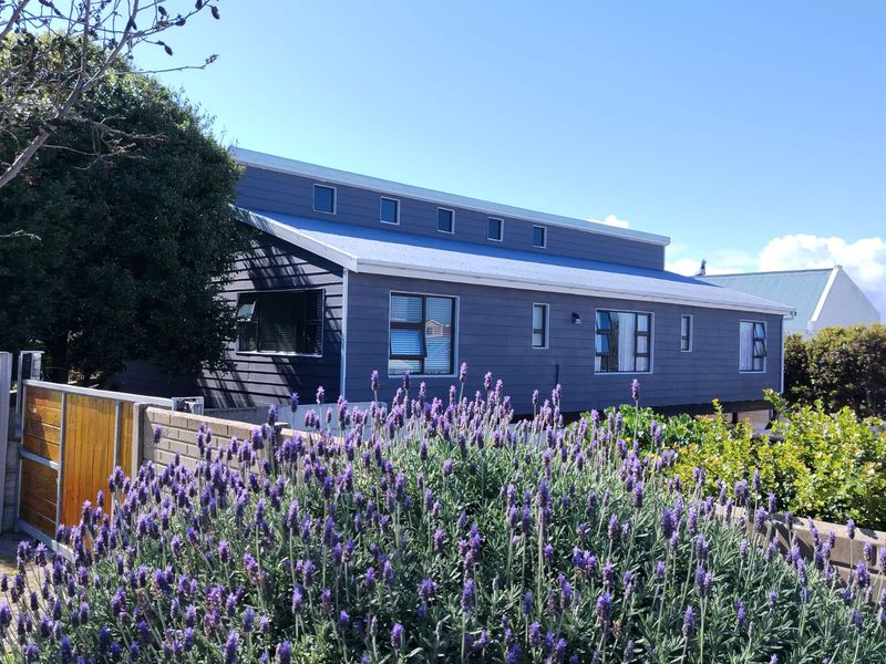 A well-maintained house exterior featuring dark timber cladding, a metal roof, and casement windows, set behind a brick boundary wall with a timber gate.